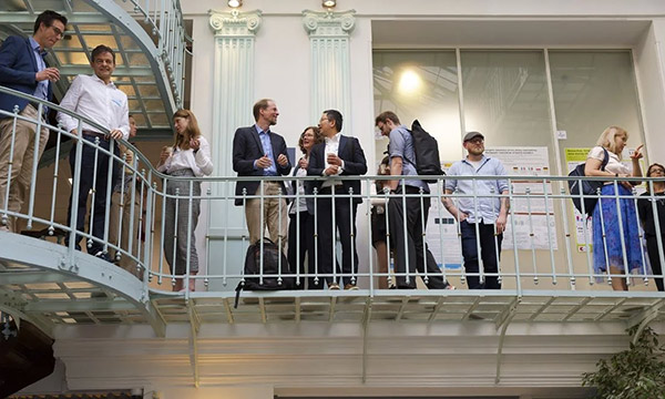 Group of people standing and talking on an indoor balcony with a spiral staircase on the left